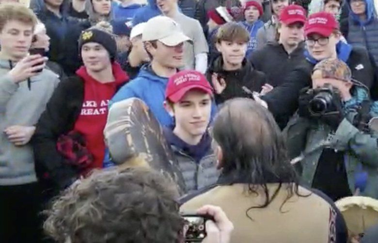 In this Friday, Jan. 18, 2019 image made from video provided by the Survival Media Agency, a teenager wearing a “Make America Great Again” hat, center left, stands in front of an elderly Native American singing and playing a drum in Washington. The Roman Catholic Diocese of Covington in Kentucky is looking into this and other videos that show youths, possibly from the diocese’s all-male Covington Catholic High School, mocking Native Americans at a rally in Washington. (Survival Media Agency via AP) NY520 NY520