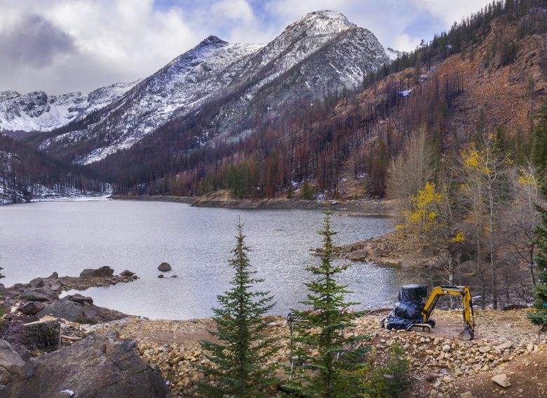 A 2017 fire scorched the landscape around Eightmile Lake in the Alpine Lakes Wilderness, prompting concerns the dam might breach. When the lake’s aging dam needed emergency repairs, the irrigation districts responsible for its maintenance flew an excavator in to fix it. Months after the repairs, the excavator remains, amid a dispute over how it should exit. (Steve Ringman / The Seattle Times)
