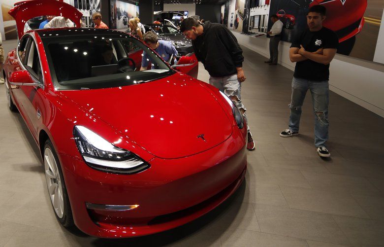 FILE- In this July 6, 2018, file photo prospective customers confer with sales associates as a Model 3 sits on display in a Tesla showroom in the Cherry Creek Mall in Denver. (AP Photo/David Zalubowski, File) 