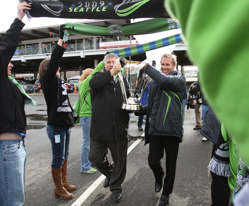 Former MLS Cup winners, Sounders head coach, Sigi Schmid and Chris Henderson walk off a ferry at the Seattle Ferry terminal carrying the MLS Cup–arriving in dramatic fashion to stir up support for this Sunday’s MLS championship game between Real Salt Lake and the L.A. Galaxy. They are walking under scarfs held by Sounders fans. (Steve Ringman / The Seattle Times)
