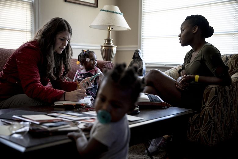 Cindy Walker writes down phone numbers of apartments for Terrineka Maxwell, right, to check out. On the sofa is Maxwell’s niece Kiya, 1. Her son, Chase, 10 months, is standing. (Andrea Morales for The Seattle Times) 