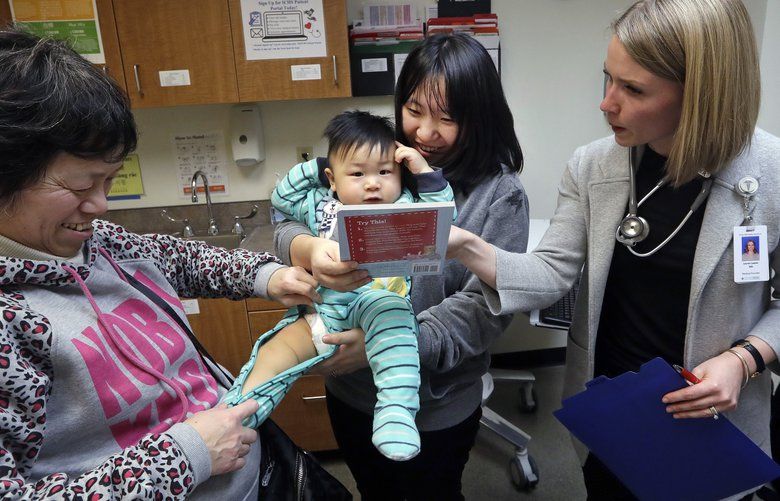 CORRECTS SPELLING OF ABEL, NOT ABLE – As his mother Wenyi Zhang holds him, one-year-old Abel Zhang looks at the book being given him by Dr. Lauren Lawler, right, as his grandmother Ding Hong helps with his clothes moments after the child received the last of three inoculations, including a vaccine for measles, mumps, and rubella (MMR), at the International Community Health Services Wednesday, Feb. 13, 2019, in Seattle. A recent measles outbreak has sickened dozens of people in the Pacific Northwest, most in Washington state and, of those, most are concentrated in Clark County, just north of Portland, Oregon. Washington Gov. Jay Inslee declared a state of emergency over the outbreak last month. (AP Photo/Elaine Thompson) WAET108 WAET108 WAET108
