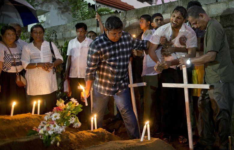 Relatives place flowers after the burial of three victims of the same family, who died at Easter Sunday bomb blast at St. Sebastian Church in Negombo, Sri Lanka, Monday, April 22, 2019. Easter Sunday bombings of churches, luxury hotels and other sites was Sri Lanka’s deadliest violence since a devastating civil war in the South Asian island nation ended a decade ago. (AP Photo/Gemunu Amarasinghe) XGA118 XGA118