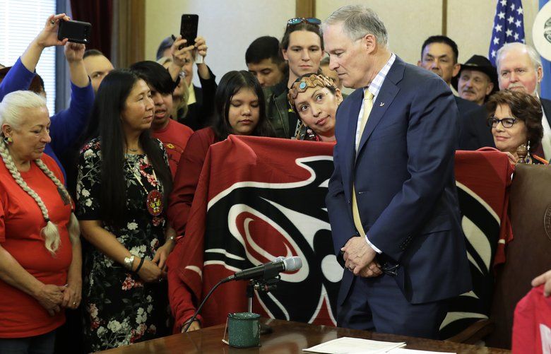 Washington Gov. Jay Inslee is presented with an honoring blanket held by Earth Feather Sovereign, center- left, of the Confederated Tribes of the Colville Reservation, after Inslee signed a bill into law, Wednesday, April 24, 2019, at the Capitol in Olympia, Wash. The bill creates liaison positions within the Washington State Patrol, and requires the agency to develop best practices in hopes of reducing disproportionate rates of violence faced by Native American and indigenous women, and also the frequency with which perpetrators of the crimes avoid justice. (AP Photo/Ted S. Warren) WATW104 WATW104
