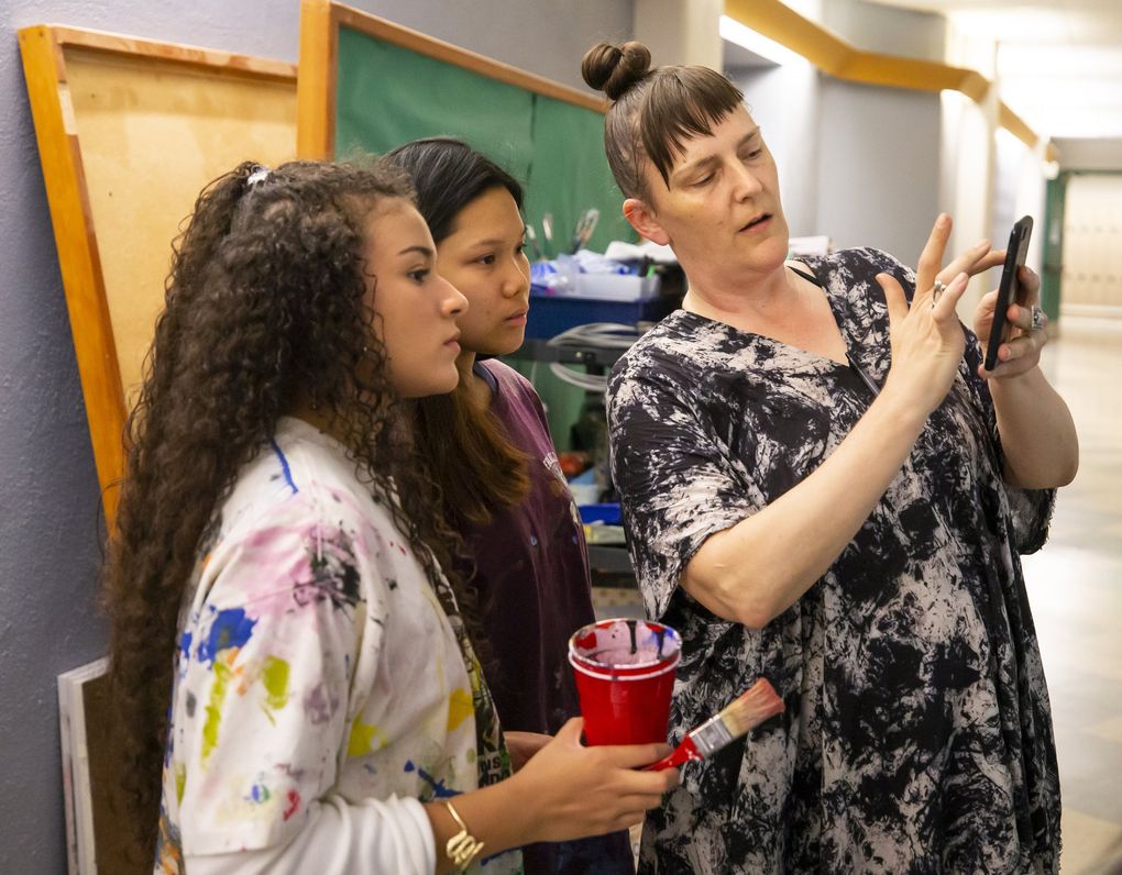 Lauren Holloway goes over designs with Tina Nguyen, 18, center, and Veronique Harris, 18, left, as students in the Art of Resistance & Resilience club at Franklin High School help create the sets for “Don’t Call it a Riot!” Holloway is a co-adviser for the club and a teaching artist at Franklin. (Bettina Hansen / The Seattle Times)