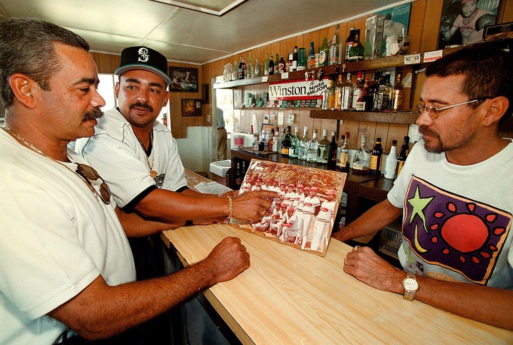 Inside La Naranja Bar, Bartender Luis Torres, Carlos Rivera, Edgar’s cousin (center), and an unidentified friend, discuss a little league photograph showing Edgar as a kid. (Juan Luis Martinez / Special for The Seattle Times)