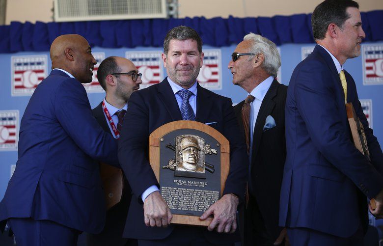 Edgar Martinez clutches his plaque as others mingle on stage after the National Baseball Hall of Fame induction ceremony end, Sunday, July 21, 2019 in Cooperstown, NY. The plaque will be hung in the hall later this evening. 210899