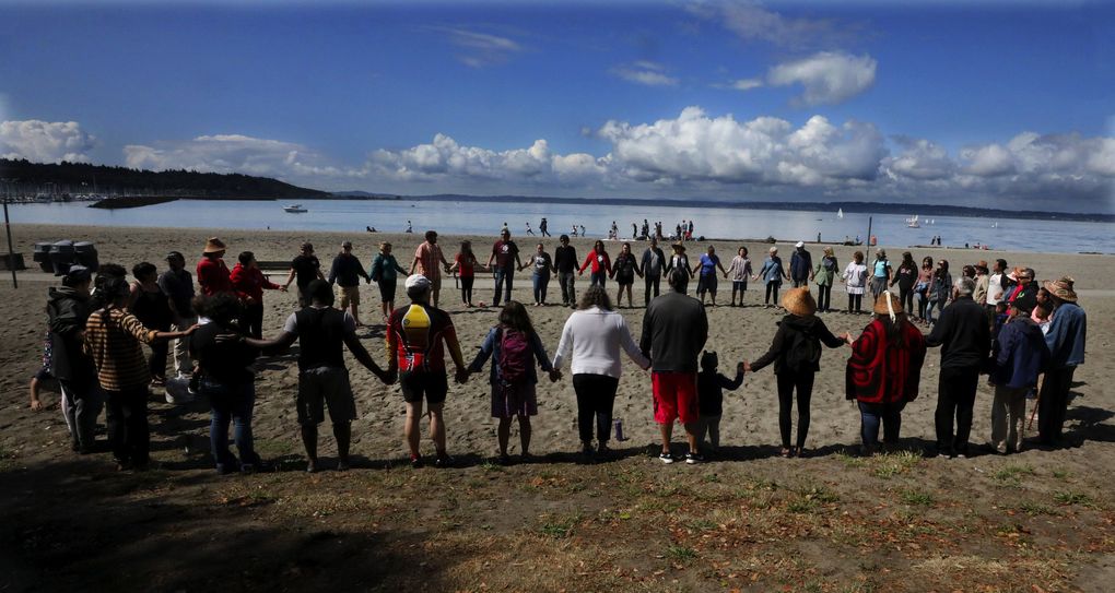 Family and friends of the Oliver family, including Marylin Oliver and Brigette Ellis, form a circle at Golden Gardens, an unofficial stop on Paddle to Lummi route, on July 19. (Alan Berner / The Seattle Times)