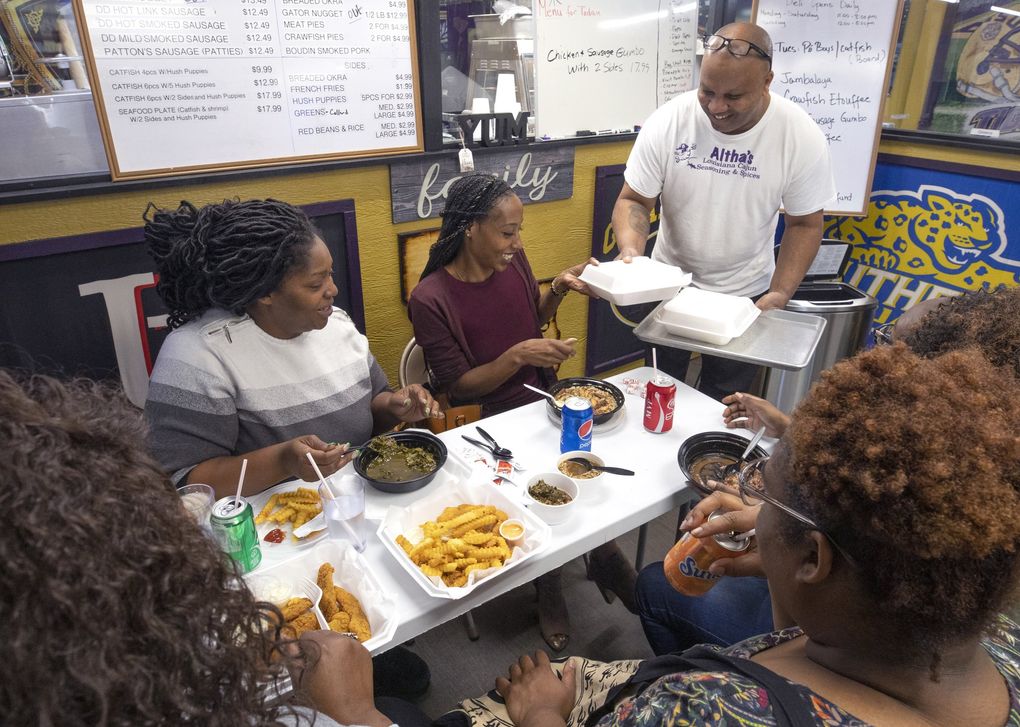 Reginald Robinson, owner of Altha’s Louisiana Cajun Seasoning, serves food to Tiniell Cato from SeaTac at his Kent store/restaurant Monday, August 26, 2019. At left is Gloria Butts of Federal Way. The friends were with others enjoying lunch.
(Ellen M. Banner / The Seattle Times)