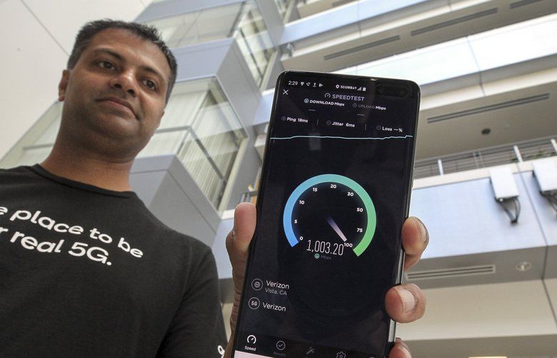 Senior Staff Engineer Vid Adiraju holds a smartphone as it goes through a 5G speed test, which shows that it has reached the level of 5G, with two commercial grade 5G millimeter network antenna boxes, background right, at the Qualcomm headquarters on Thursday, Aug. 1, 2019 in San Diego, Calif. (Hayne Palmour IV/THe San Diego Union-Tribune/TNS)  1406573 1406573