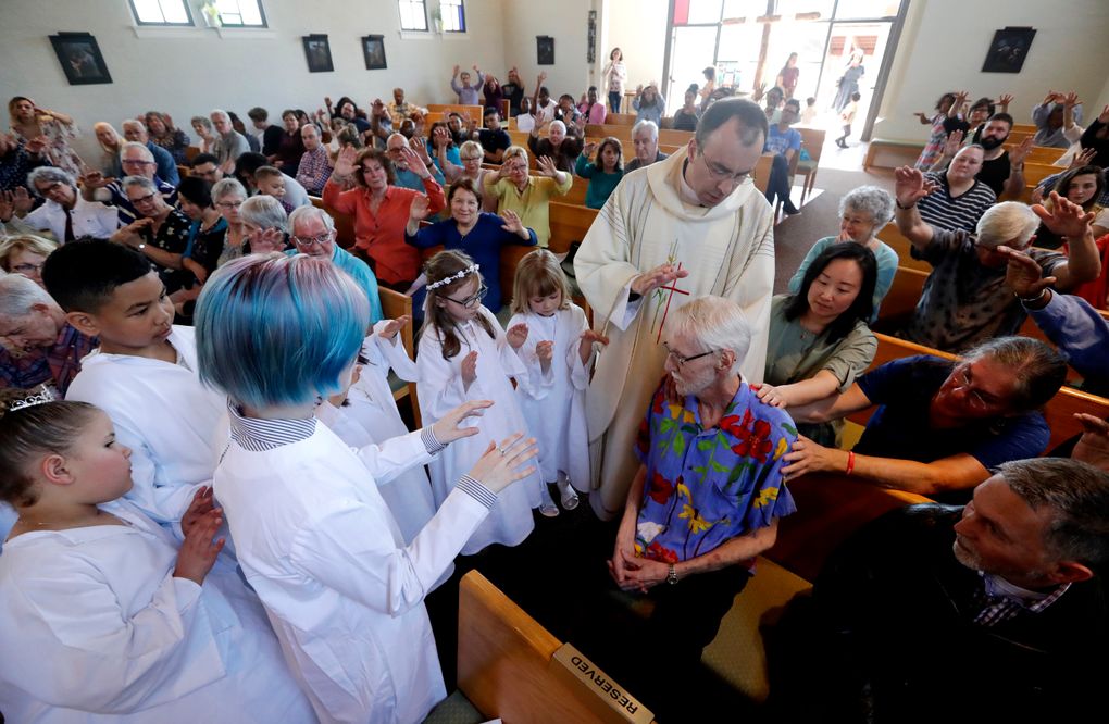 Robert Fuller, seated center right, receives a blessing and prayer from Rev. Quentin Dupont and white-robed children who had just received their first communion at St. Therese Parish Catholic church in Seattle. (AP Photo/Elaine Thompson)