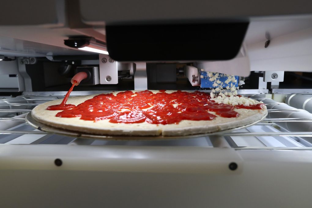 Sauce is squirted and cheese dropped on a pizza in an automated assembly platform designed for the hospitality industries at Seattle-based Picnic. (Ken Lambert / The Seattle Times)