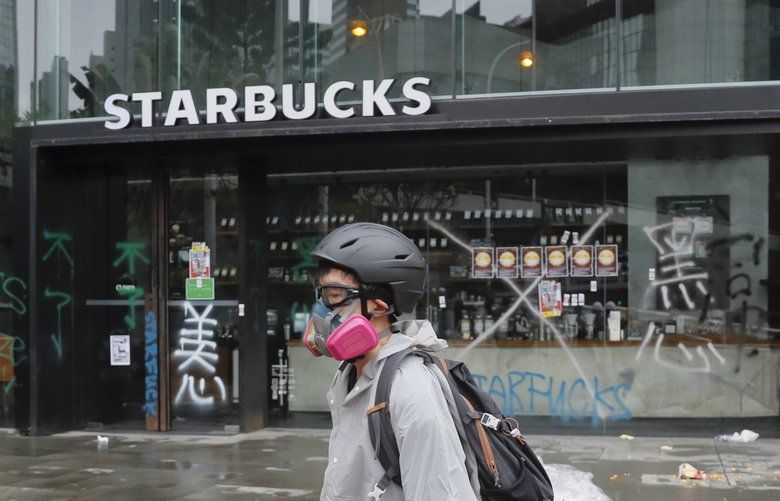 A protestor walks past a vandalized Starbucks outlet in Hong Kong, Sunday, Oct. 6, 2019. Shouting “Wearing mask is not a crime,” tens of thousands of protesters braved the rain Sunday to march in central Hong Kong as a court rejected a second legal attempt to block a mask ban aimed at quashing violence during four months of pro-democracy rallies. (AP Photo/Kin Cheung) KC2907 KC2907