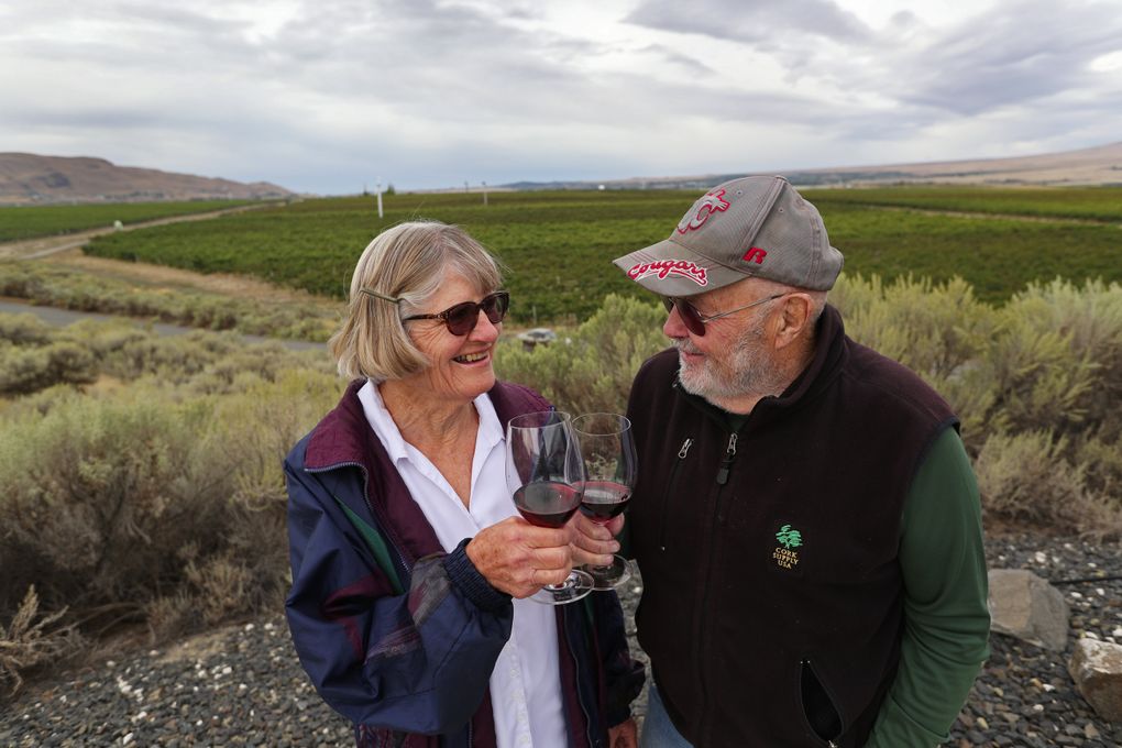 Back in 1975, married couple John and Ann Williams, along with others, planted many of the grapes seen in the background at what is now Kiona Vineyards in the Red Mountain AVA. Retired now and in their 80s, the couple toasts with a 2016 Kiona Sangiovese. Their son Scott, who has been running Kiona while acquiring more vineyards on Red Mountain, also gets a lot of help from his sons, JJ and Tyler. (Ken Lambert / The Seattle Times)