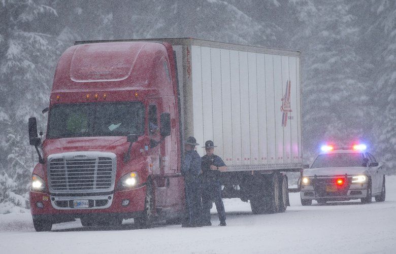 Oregon State Police talk with a truck driver who was traveling without chains near Willamette Pass east of Oakridge, Ore., on Monday, Nov. 25, 2019. (Andy Nelson/The Register-Guard via AP) 