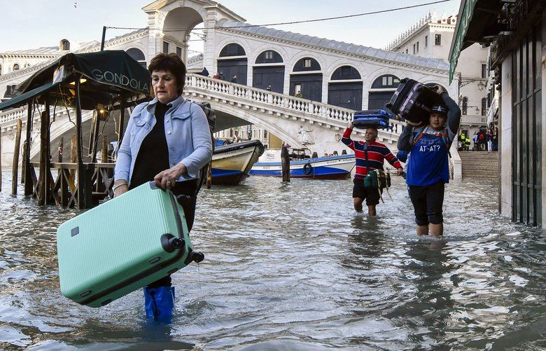 People carry their luggage as they wade through water during a high tide of 1.44 meters (4.72 feet), near the Rialto Bridge, in Venice, Italy, Monday, Dec. 23, 2019. Venice is facing more intense floods on Monday, while it battles to recover from the exceptional high tide that hit it in November, causing massive damages. (AP Photo/Luigi Costantini) VEN103 VEN103