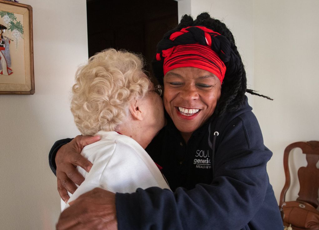 While on her rounds, Fai Mathews, right, shares a hug with Helen Rekow. Mathews delivers food to Rekow, but the two also talk about about the city, their health and life. (Ellen M. Banner / The Seattle Times)