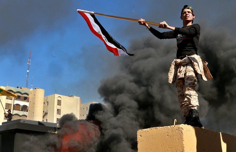Protesters burn property as a militiaman waves an Iraqi flag in front of the U.S. embassy compound, in Baghdad, Iraq, Tuesday, Dec. 31, 2019. Dozens of angry Iraqi Shiite militia supporters broke into the U.S. Embassy compound in Baghdad on Tuesday after smashing a main door and setting fire to a reception area, prompting tear gas and sounds of gunfire. (AP Photo/Khalid Mohammed) BKM128 BKM128