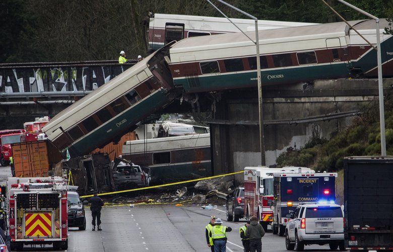 A car at left center on an Amtrak southbound train appears to be resting on an overturned train car that is laying in the southbound lanes of I-5 after the train derails south of Mounts Road SW overpass  Monday morning, December 18, 2017.