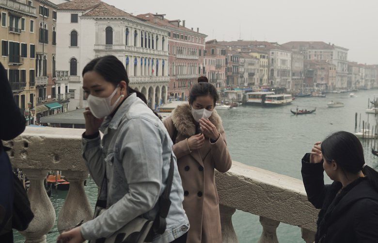 Tourists fiddle with their protective face masks take selfies atop Rialto bridge in Venice, Italy, Tuesday, Feb. 25, 2020. Italy has been scrambling to check the spread of Europe’s first major outbreak of the new viral disease amid rapidly rising numbers of infections and calling off the popular Venice Carnival and closing tourist attractions.(AP Photo/Renata Brito) XRB115 XRB115