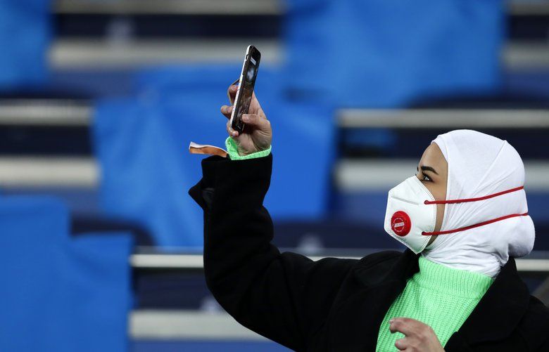 A fan wearing a protective mask takes a picture with her cell phone prior the Champions League, round of 16, first leg soccer match between Real Madrid and Manchester City at the Santiago Bernabeu stadium in Madrid, Spain, Wednesday, Feb. 26, 2020. (AP Photo/Manu Fernandez) XDMV101 XDMV101