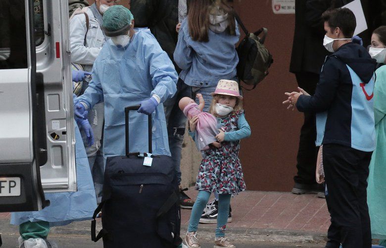 Health personnel wearing protection clothing assist guests as they leave the H10 Costa Adeje Palace hotel in La Caleta, in the Canary Island of Tenerife, Spain, Friday Feb. 28, 2020. Some guests have started to leave the locked down hotel after undergoing screening for the new virus that is infecting hundreds worldwide. (AP Photo/Joan Mateu) EM104 EM104