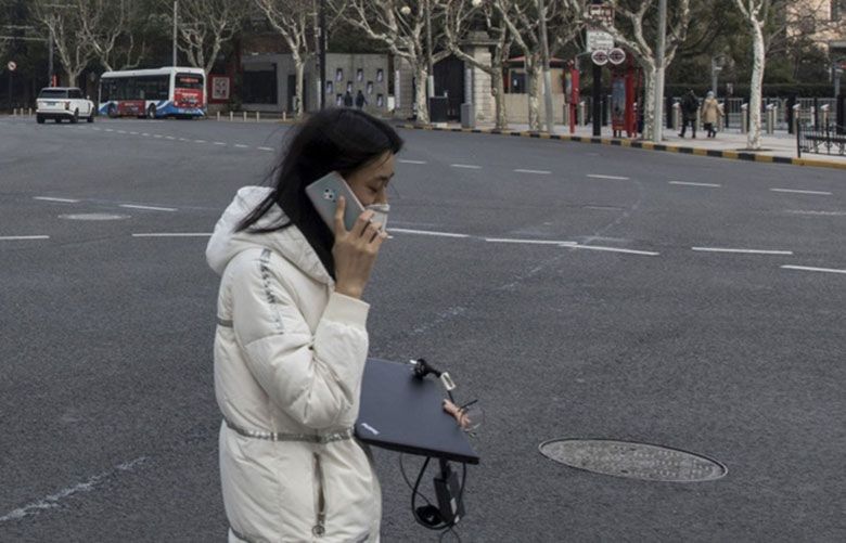 A woman carrying a laptop crosses an almost empty street in Shanghai on Jan. 29. (Bloomberg photo by Qilai Shen).