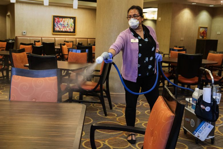 Maria Johnson, environmental services director at Aljoya Mercer Island retirement community, disinfects the dining room.  After about 10 minutes, the tables and chairs are all wiped down. This procedure used to be done only once a day in this room and other communal areas, but now is being stepped up to twice a day.  (Ellen M. Banner / The Seattle Times)