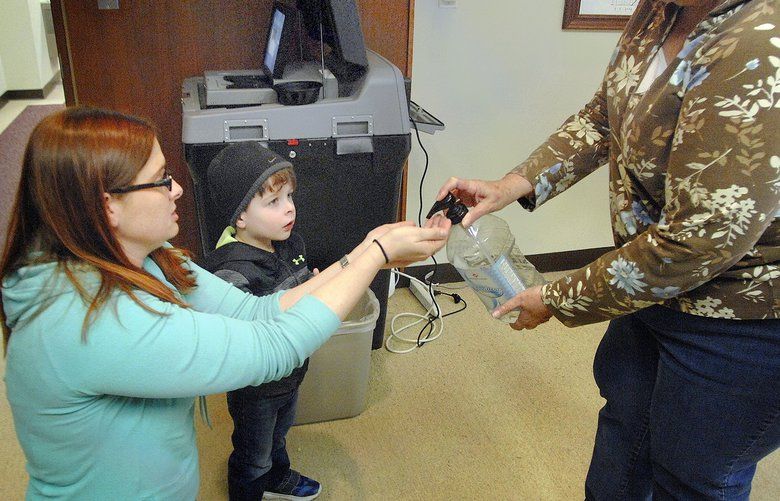 Bloomington Election Commission Judge Kim Osterbrock, right, squeezes hand sanitizer for voter Angela Kuppersmith and her son, Wyatt, 3, after they cast their early vote Tuesday, March 10, 2020, at the Government Center in Bloomington. Election officials are prepared to help keep voters safe for the primary election next Tuesday with the possibility of a looming coronavirus hanging over Illinois.  (David Proeber/The Pantagraph via AP) ILBLO101 ILBLO101