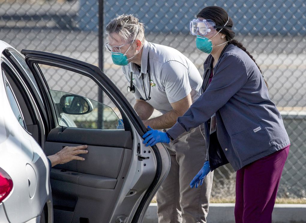 Advanced registered nurse practitioner Justin Stoltzfus, middle, and medical assistant Blanca Quintero speak with a patient who came in with flu-like symptoms for testing at a parking lot site set up at the Quincy Community Health Center. Staff can test a specimen for the flu at the clinic, and specimen can be sent to other laboratories for coronavirus testing. (Amanda Snyder / The Seattle Times)
