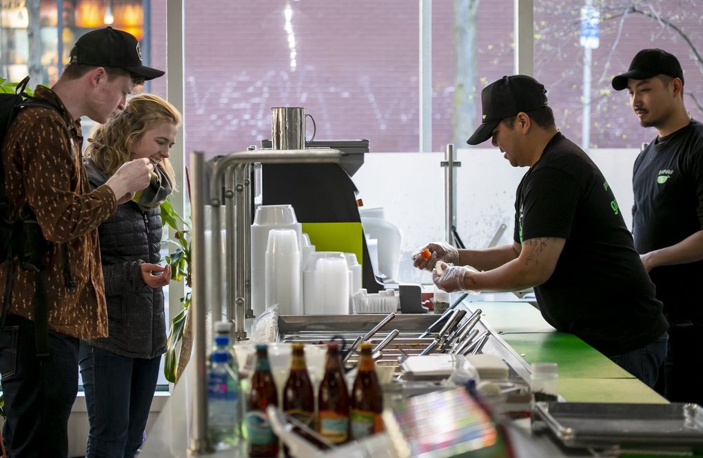 Robert Humber, left, and Jessica Pereversoff, of Vancouver, order meals to go from Richard Phakeovilay and Jason Lee at goPoke in the Chinatown-International District Monday. The restaurant, owned by a family from Hawaii, is offering everything on their menu for to-go orders and on various apps to comply with the restaurants ban announced by Gov. Jay Inslee. (Erika Schultz / The Seattle Times)
