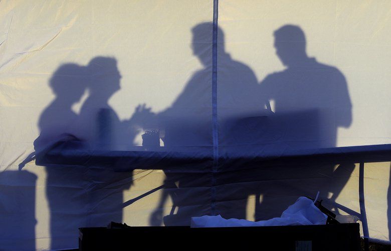 Medical personnel are silhouetted against the back of a tent before the start of coronavirus testing in the parking lot outside of Raymond James Stadium early Wednesday, March 25, 2020, in Tampa, Fla. The testing is being done by appointment only. (AP Photo/Chris O’Meara) FLCO101 FLCO101