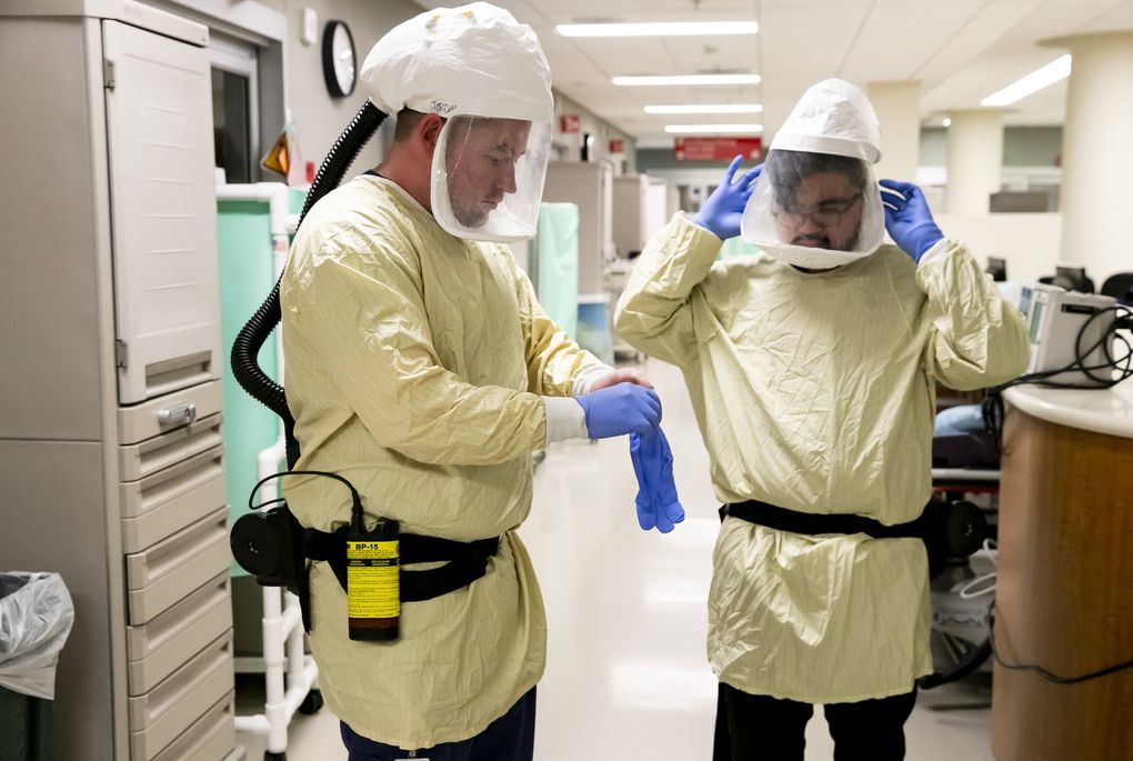 Registered nurse Blake Baldwin, left, and ER tech Abe I. Inton show how to put on a powered air purifying respirator (PAPR) at EvergreenHealth’s emergency department and critical care unit in Kirkland on Tuesday. The respirators help provide protection from potentially contaminated air for medical staff when they are in negative airflow environments. Nurses, doctors and techs wear the respirators when working with patients with COVID-19 symptoms. (Erika Schultz / The Seattle Times)