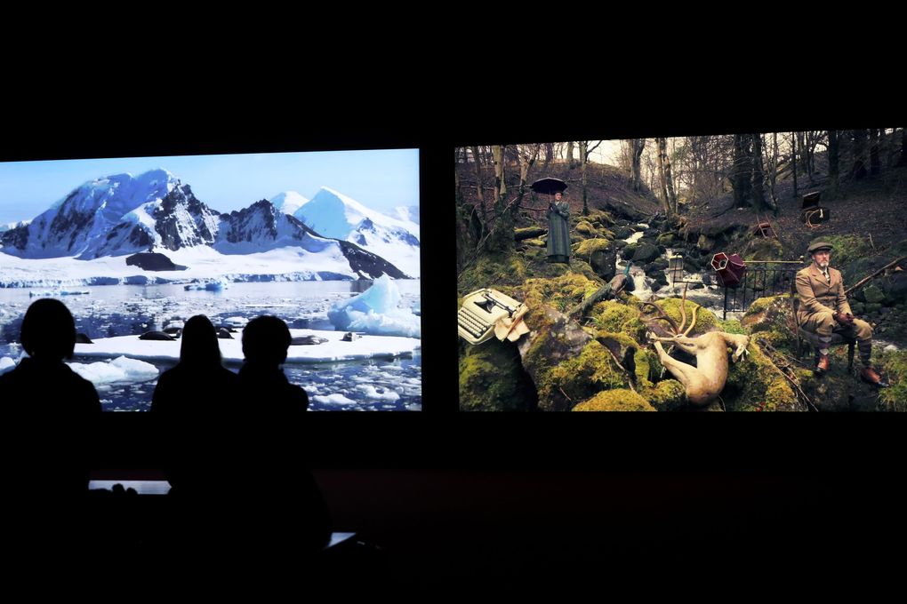 Seattle Art Museum visitors watch “Vertigo Sea” (2015), a film showing as part of the “John Akomfrah: Future History,” exhibit. The film is split into three screens showing simultaneous images; only two screens are seen here. (Ken Lambert / The Seattle Times)