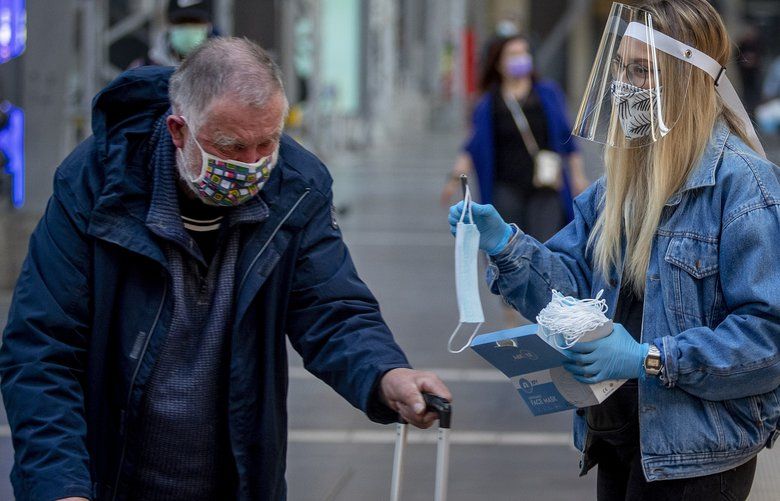 A woman working for the regional public transport company offers a face mask to an elderly man in the main train station in Frankfurt, Germany, Monday, April 27, 2020. To avoid the spread out of the coronavirus face masks are mandatory in shops and public transport in the federal state Hesse from Monday on. (AP Photo/Michael Probst) PFRA104 PFRA104