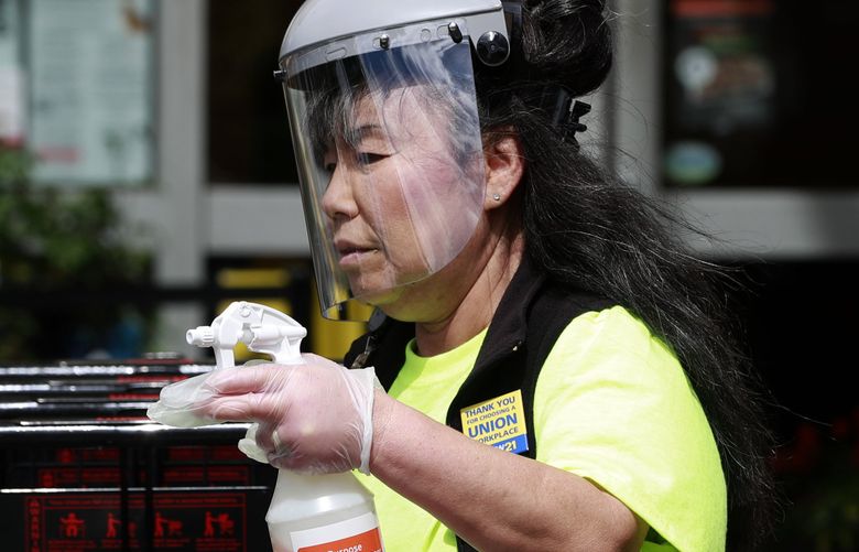 Kyong Barry, Albertsons front end manager, disinfects shopping carts for customers during a busy afternoon rush at the store in Auburn, Wash. Monday, April 27, 2020.  213765 (Erika Schultz / The Seattle Times)