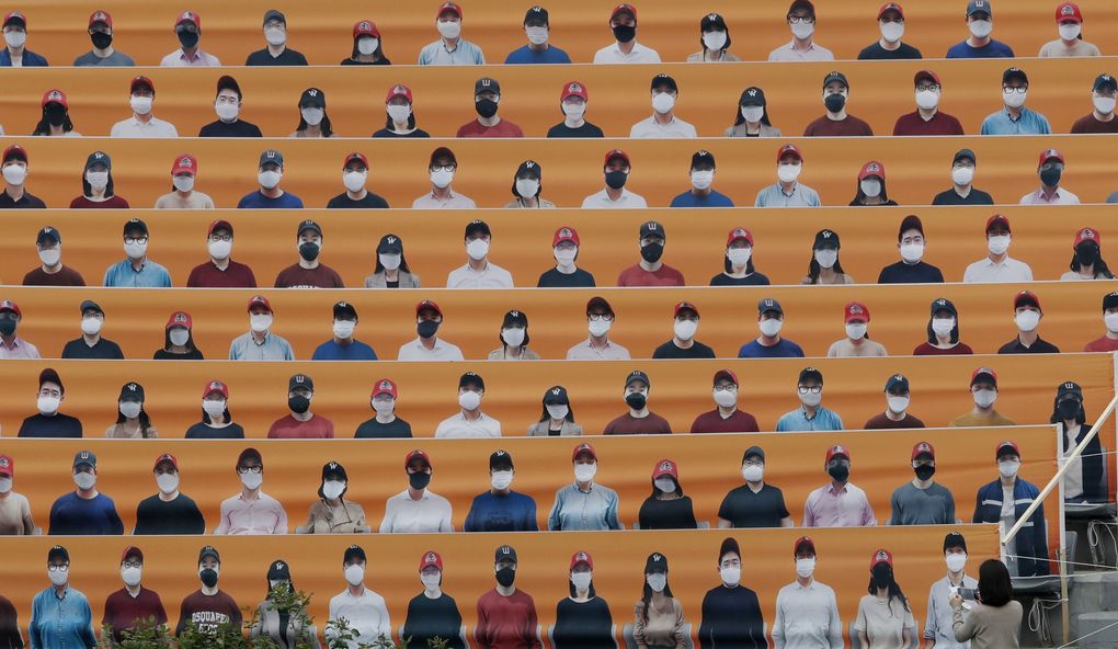 A woman holds her smartphone in front of the spectators’ seats which are covered with pictures of fans, before the start of a baseball game between Hanwha Eagles and SK Wyverns in Incheon, South Korea, May 5. (Lee Jin-man / The Associated Press)