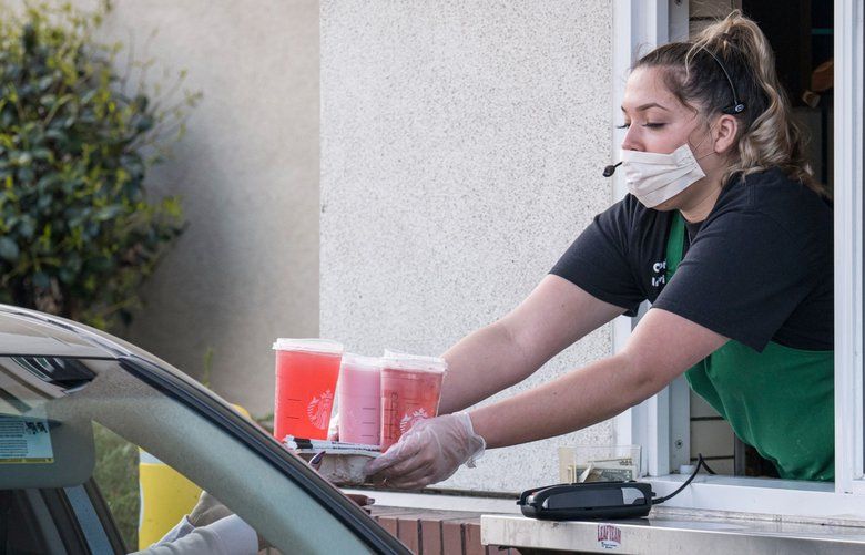 A Starbucks Corp. employee wearing a protective mask and gloves hands a customer an order from a drive-thru window at a store in Hercules, California, U.S., on Tuesday, April 7, 2020. Some of America’s fast-food workers are finally getting face masks and emergency sick days to help get them through the coronavirus outbreak. Photographer: David Paul Morris/Bloomberg