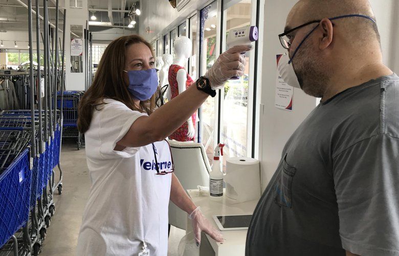 Goodwill employee Isabel Esnard checks the temperature of a customer as he enters the store during the first day of reopening of non-essential stores in Miami-Dade County at the Goodwill Bird Ludlam store on May 18, 2020 in Miami. (Jose A. Iglesias/Miami Herald/TNS)  1665381 1665381 1665381