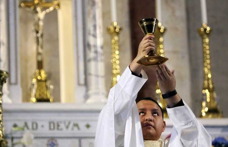 In this April 19, 2020, photo, the Rev. Joseph Dutan, 32, lifts the chalice during Sunday Mass at an empty St. Brigid Church in the Brooklyn borough of New York. Dutan recalls how he lifted the chalice in the empty church and felt a flood of emotions: grief, the pain of isolation, even doubt. But also, the promise of hope that is the gift of every Easter — even in the midst of a pandemic that had already robbed him and his community of so much, and threatened to take so much more. (AP Photo/Jessie Wardarski) NYJW103 NYJW103