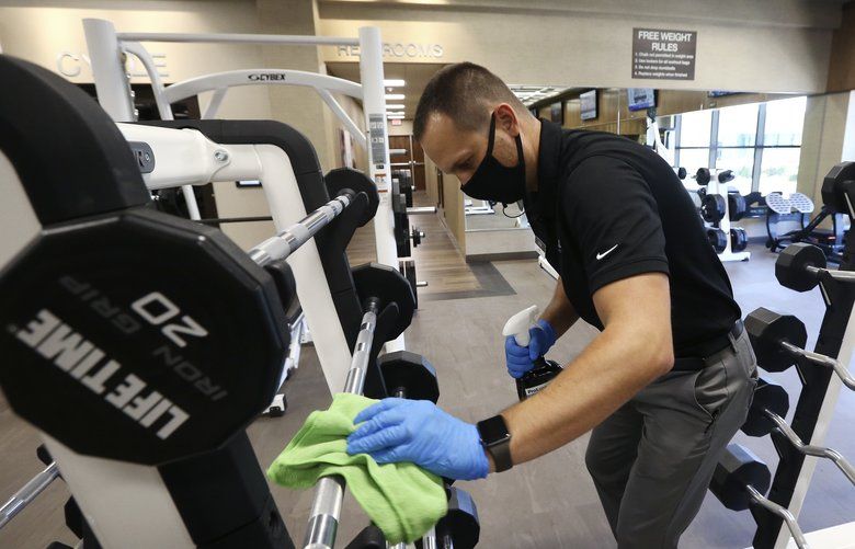 Jason Nichols, facilities operation manager, disinfects equipment at the Life Time Biltmore as it opens for business after being closed due to the coronavirus Monday, May 18, 2020, in Phoenix.  Big-box gyms and local fitness studios are reopening under a patchwork of protocols based on state and local guidance, but most are following these basics: spacing out cardio machines, touchless entry, smaller class sizes, increased cleaning and requiring users to clean all equipment before and after each use. (AP Photo/Ross D. Franklin) AZRF202 AZRF202