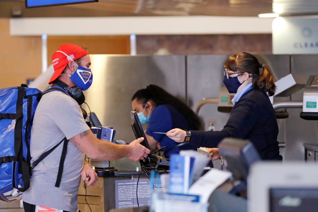 Fish industry worker Tucker Uruski, left, checks his bags for a trip to Alaska at Seattle-Tacoma International Airport, May 18, 2020. The airport now requires travelers to wear face coverings in the public areas there. The Port of Seattle has encouraged its employees to wear face coverings, and all federal agencies that operate at the airport require their employees to wear them. All airlines operating at Sea-Tac require employees and passengers to wear face coverings. (The Associated Press / Elaine Thompson)