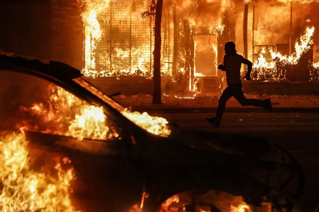 In this Associated Press photo from May 30, a protester runs past burning cars and buildings on Chicago Avenue in St. Paul, Minnesota. (John Minchillo / The Associated Press)