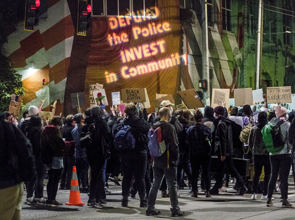 The core of many protesters’ demands, indicated by a slogan projected recently on a wall at Pine Street and 11th Avenue, is to transfer money, responsibility and power from police to the community. (Amanda Snyder / The Seattle Times)