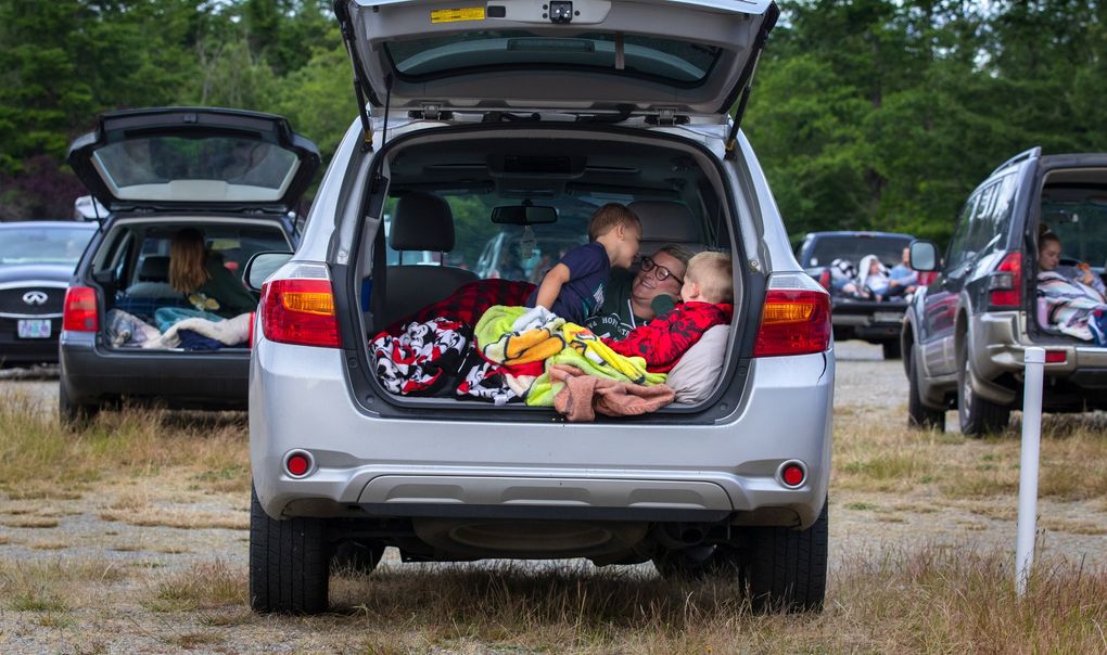 Logan Miller, 6, whispers something to his mom, Cassie, as brother Easton, 9, sits at right in the family car as they settle in before “The Goonies” starts at the Skyline Drive-In in Shelton. (Ellen M. Banner / The Seattle Times)