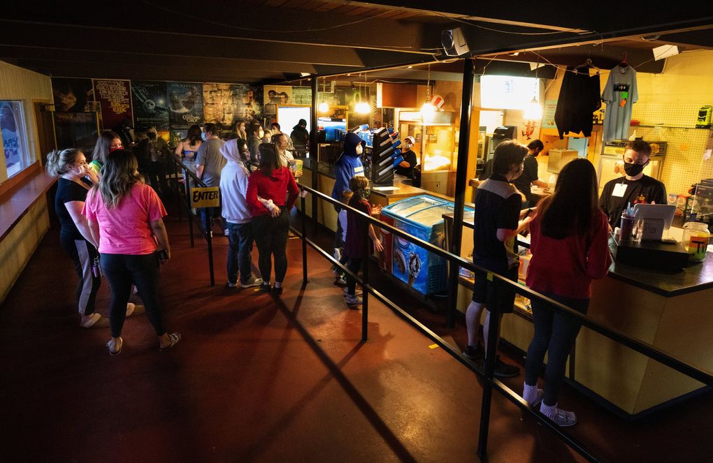 Cashier Chase Rollins, right, waits on customers in the snack bar at the Skyline Drive-In in Shelton. Customers are only allowed to enter the snack bar through one door, must practice social distancing while in line, wear masks and exit through another door. (Ellen M. Banner / The Seattle Times)