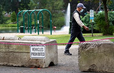 A person wearing a face mask walks past the concrete barriers at Lake Sacajawea to block vehicles from Martin Dock, where an unpermitted gathering is scheduled to take place on July 4.