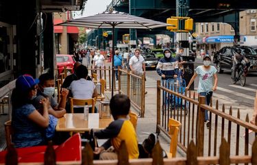 Pedestrians wearing protective masks pass in front of customers sitting outside to eat at a restaurant in the Corona neighborhood in the Queens borough of New York on June 27, 2020. MUST CREDIT: Bloomberg photo by Amir Hamja.