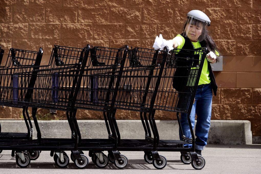 Kyong Barry, Albertsons front-end manager in Auburn, disinfects shopping charts. Women represent 63% of Seattle metro area workers in occupations deemed essential, including grocery workers. (Erika Schultz / The Seattle Times)