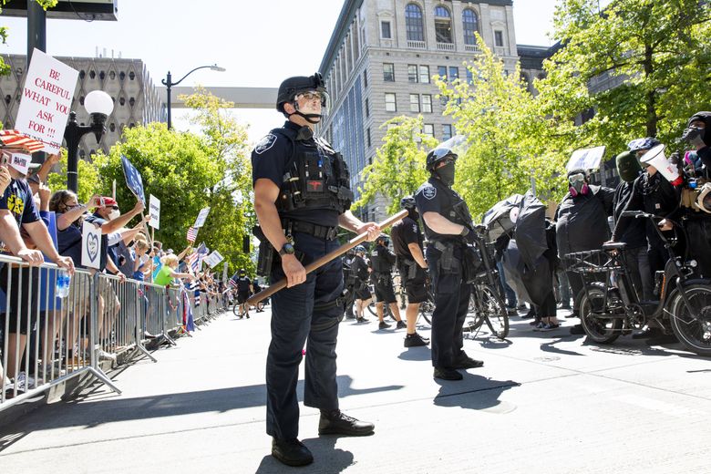 Seattle Police hold a line on Fourth Avenue between protesters supporting the Seattle Police Officers Guild, or SPOG, on the left, and counter protesters on the right, during SPOG’s rally at Seattle City Hall to speak out against the defunding of their department Sunday. (Bettina Hansen / The Seattle Times)